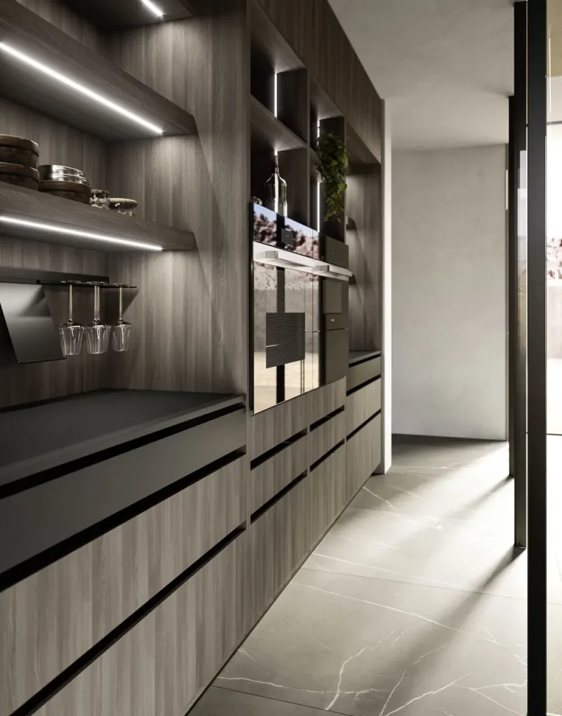 Modern kitchen with dark wood cabinetry, built-in ovens, and open shelves; wine glasses hang beneath a shelf and under-cabinet lighting.
