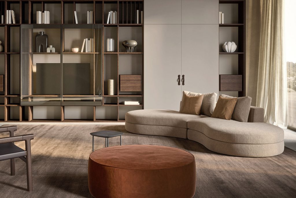Modern living room featuring a dark wood grid shelving unit, a light curved sectional sofa with beige cushions, and a round brown ottoman.