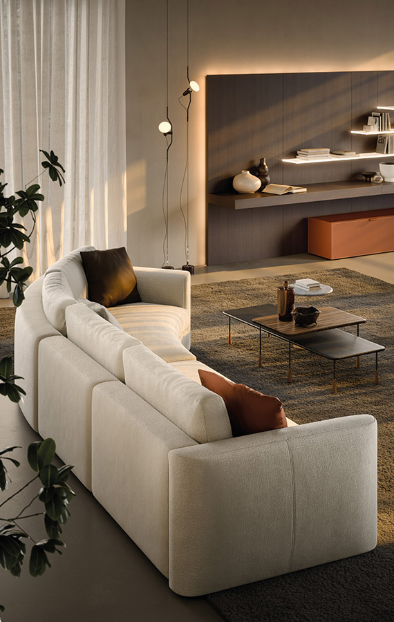 Cream sectional sofa with brown pillows in a contemporary living room, with a low coffee table and warm wall lighting.