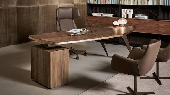 Executive office scene with a curved wooden desk, high-back leather chair, and two brown lounge chairs facing the desk, set against a wood-paneled wall and bookshelves.