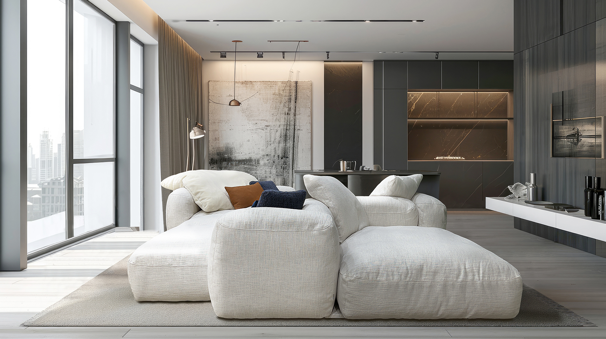 Open-concept living room with a light gray sectional, soft cushions, and a dark marble kitchen along the back wall; large windows overlook a city skyline