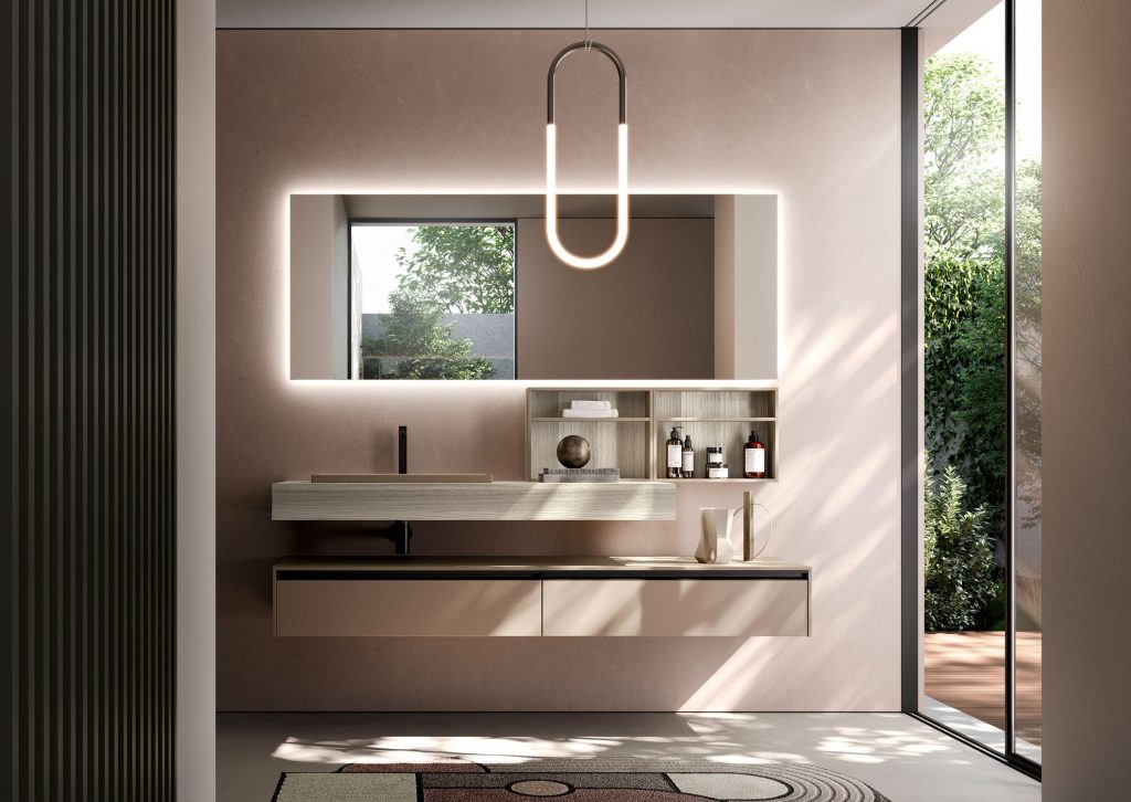 Modern bathroom with a backlit rectangular mirror, floating sink, and open shelving above a beige vanity. The space is lit by a pendant oval light and natural daylight from a large window/door to greenery.