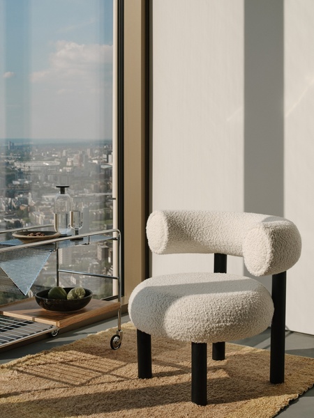 Sunlit modern white textured chair by a large window, with a small serving cart holding a wine glass and plate nearby.