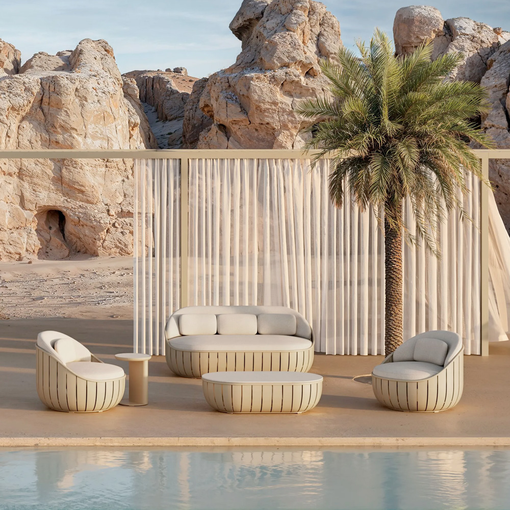 Modern beige outdoor lounge set by a pool, with cushioned rounded chairs and a matching coffee table, a palm tree, and rocky desert backdrop.